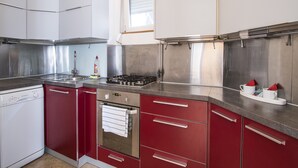 Una cocina moderna con electrodomésticos de acero inoxidable, armarios rojos y un ventanal con persianas.