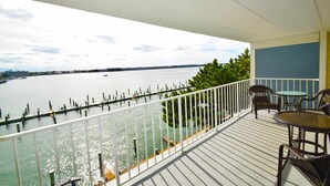 Un balcon offrant une vue sur une étendue d’eau paisible, un quai et une côte lointaine.
