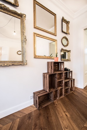 A hallway with wooden flooring, a series of mirrors with ornate frames, and a rustic wooden shelving unit.