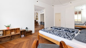 A modern bedroom with a wooden bed, built-in shelves, a mirror, and a view into the dining area.