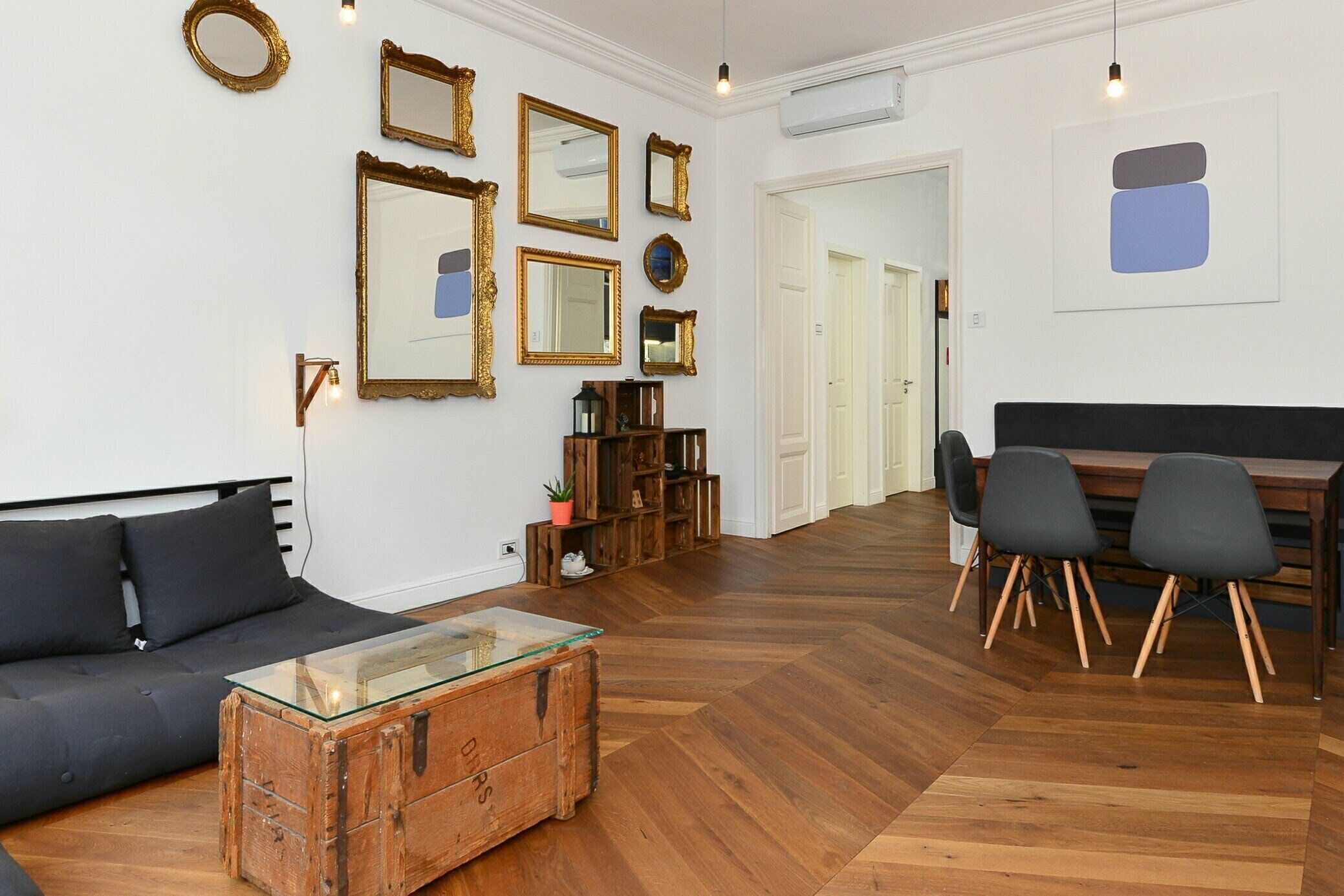 A modern living room with a sofa, a glass-top coffee table, wooden flooring, and a dining area with chairs and a table.
