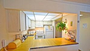 A compact kitchen with white cabinets, a wooden countertop, a microwave, an oven, and a refrigerator. - Ocean Hideaway 202 (Ocean City)