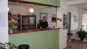 A reception area with a green wall, a wooden counter, a refrigerator, and a potted plant.