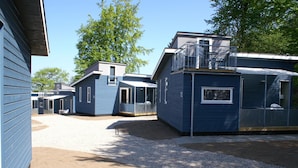 Une rangée de cabanes bleues, avec une allée en gravier et des arbres en arrière-plan.
