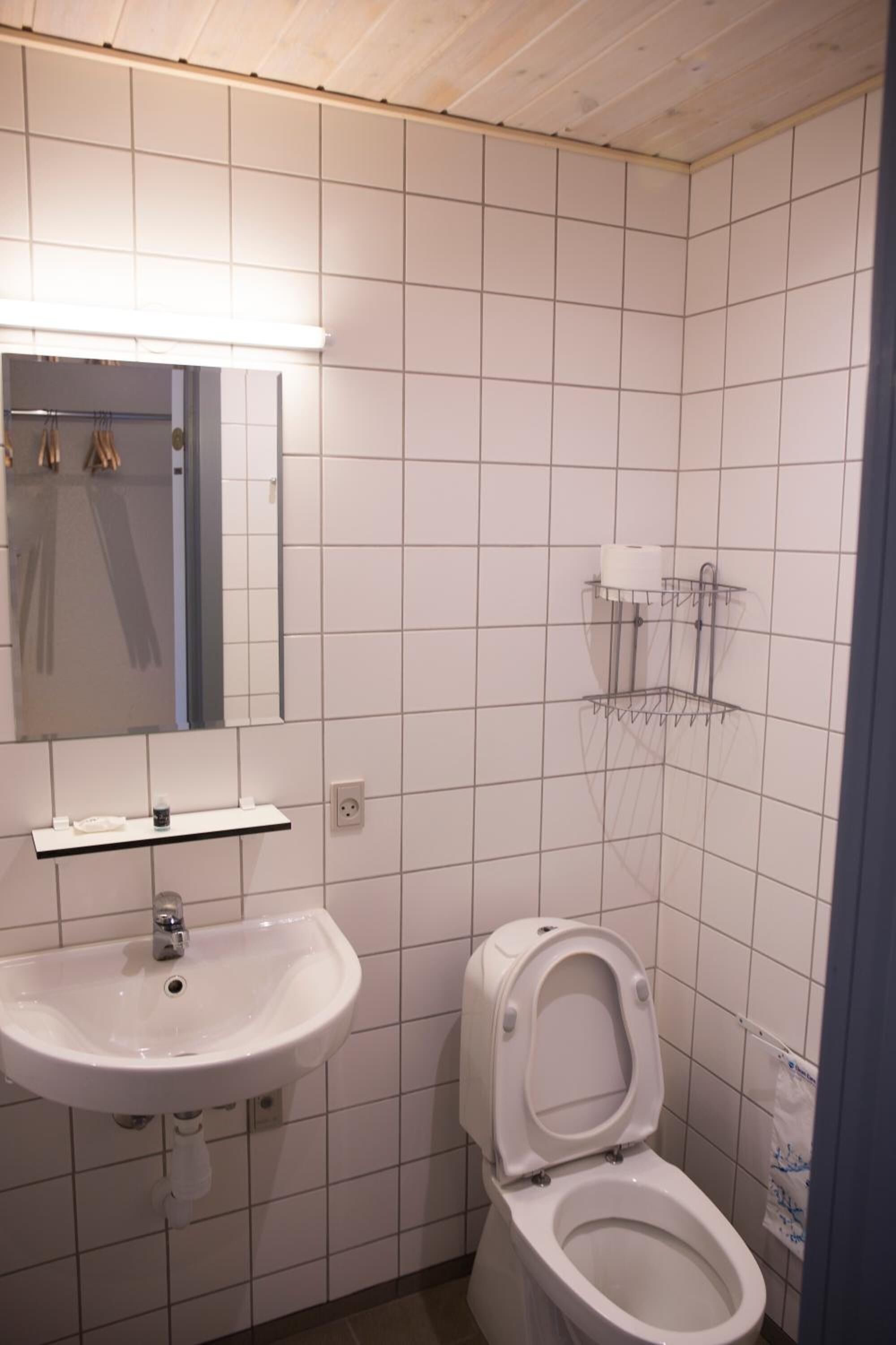 A bathroom with white tiles, a sink, a toilet, a mirror, and a towel rack.
