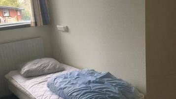 Un lit simple avec un matelas matelassé et un oreiller, une fenêtre avec des rideaux et un radiateur.