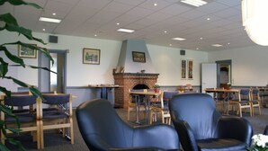 Une pièce avec une cheminée en briques, des chaises en bois, une table et un plafond doté d’un éclairage encastré.