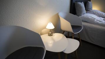 Una habitación de hotel con una cama, dos sillas blancas y una mesa con una lámpara.