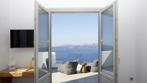 Ein Schlafzimmer mit Bett, Schreibtisch, Fernseher und Meerblick durch eine Glastür.