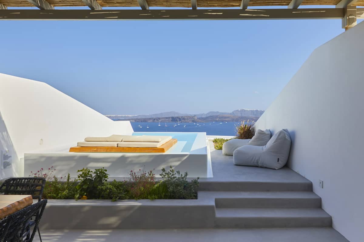 Un espace de détente extérieur moderne avec vue sur la mer, comprenant un canapé, un banc en bois et des marches menant à une plateforme surélevée.