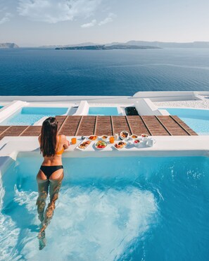 A woman in a pool with a table of food and drinks in the background. - Phōs The Boutique Luxury Hotel & Villas (Santorini)