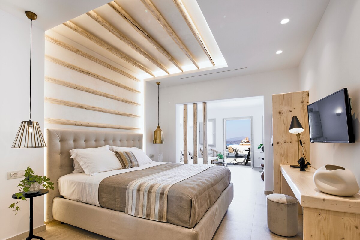 A modern bedroom with a large bed, a desk with a TV, and a view of the outdoors.