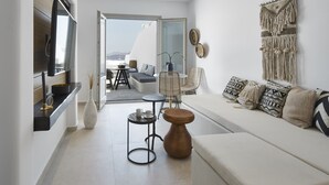 Ein modernes Wohnzimmer mit einer Couch, einem Couchtisch und einem an der Wand befestigten Fernseher. Es gibt einen Balkon mit Meerblick.