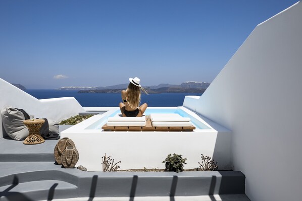 A person relaxing on a white infinity pool with a view of the sea and distant mountains. - Phōs The Boutique Luxury Hotel & Villas (Santorini)