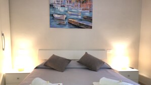 A neatly made bed with pillows, a painting of boats on the wall, and a nightstand with a lamp. - Volì club Bed & Breakfast (Siderno)