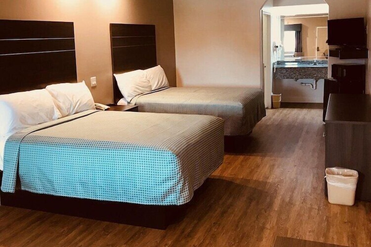 Habitació d'hotel amb dos llits, un escriptori, una cadira i una cuineta.