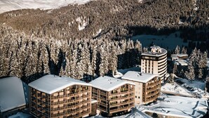 A modern hotel complex with multiple buildings, surrounded by snow-covered trees and mountains in the background.