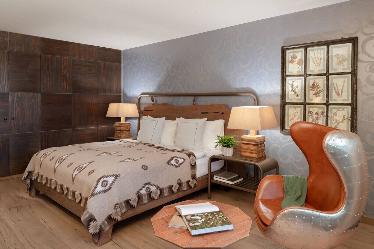 A bedroom with a bed, two bedside tables, a chair, and a wall with framed botanical prints.