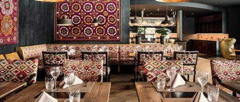 A restaurant with wooden tables and benches, patterned cushions, and hanging pendant lights.