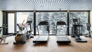 A gym with treadmills, elliptical machines, and a rowing machine, with large windows offering a snowy forest view.