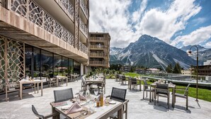 An outdoor dining area with tables and chairs, set against a backdrop of mountains and a clear sky.