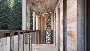 A wooden deck with glass railings, leading to a covered area with a view of trees.