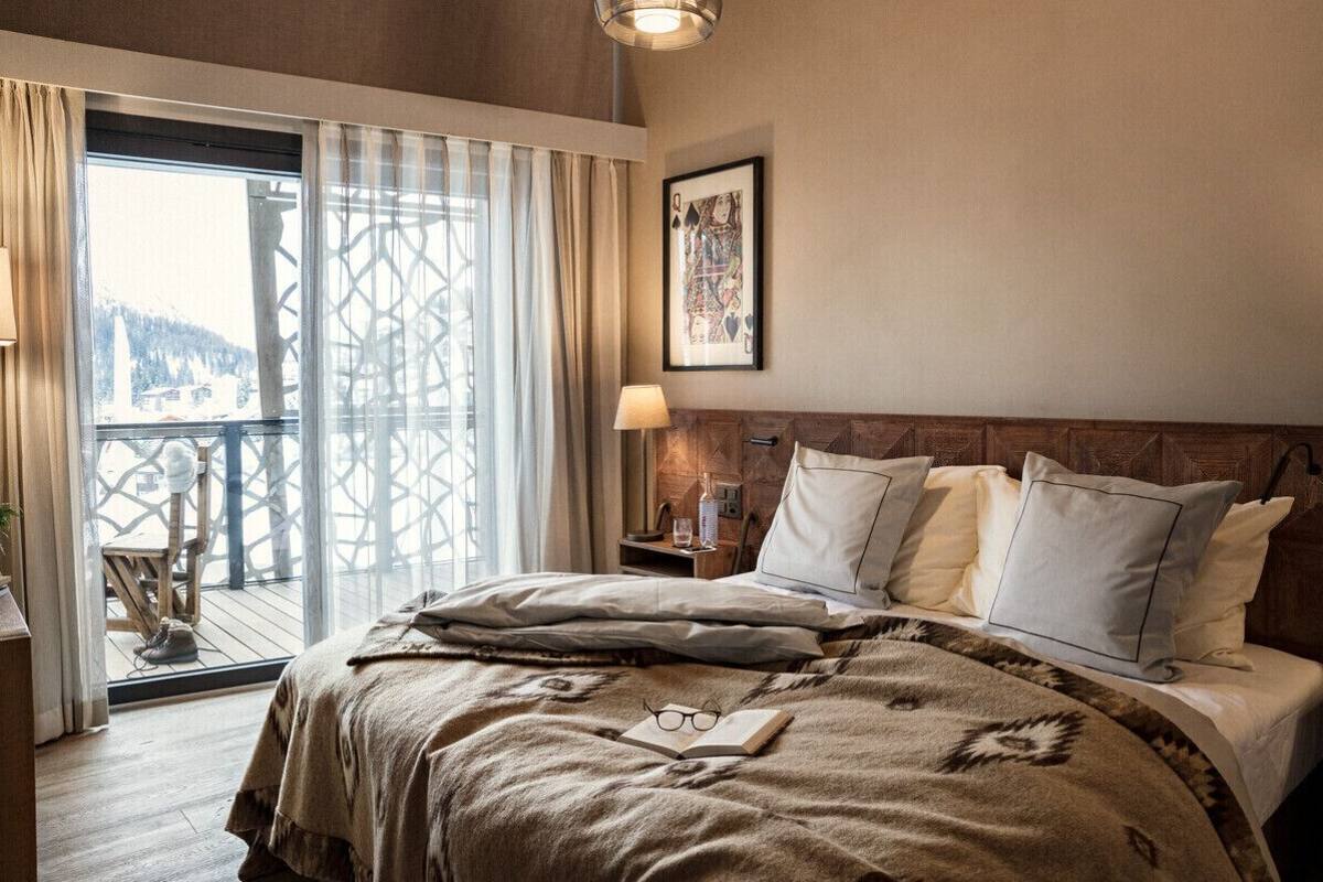 A hotel room with a large bed, a wooden headboard, a balcony with a view, and a framed picture on the wall.