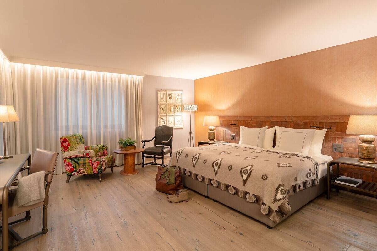 A hotel room with a large bed, a desk, a chair, and a small table with a plant.