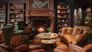 A cozy living room with leather furniture, a fireplace, bookshelves, and decorative plants.