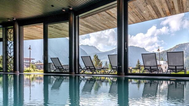 An indoor swimming pool with lounge chairs and a view of mountains.