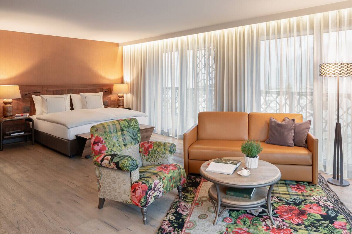 A hotel room with a bed, a sofa, a chair, a coffee table, and a lamp.