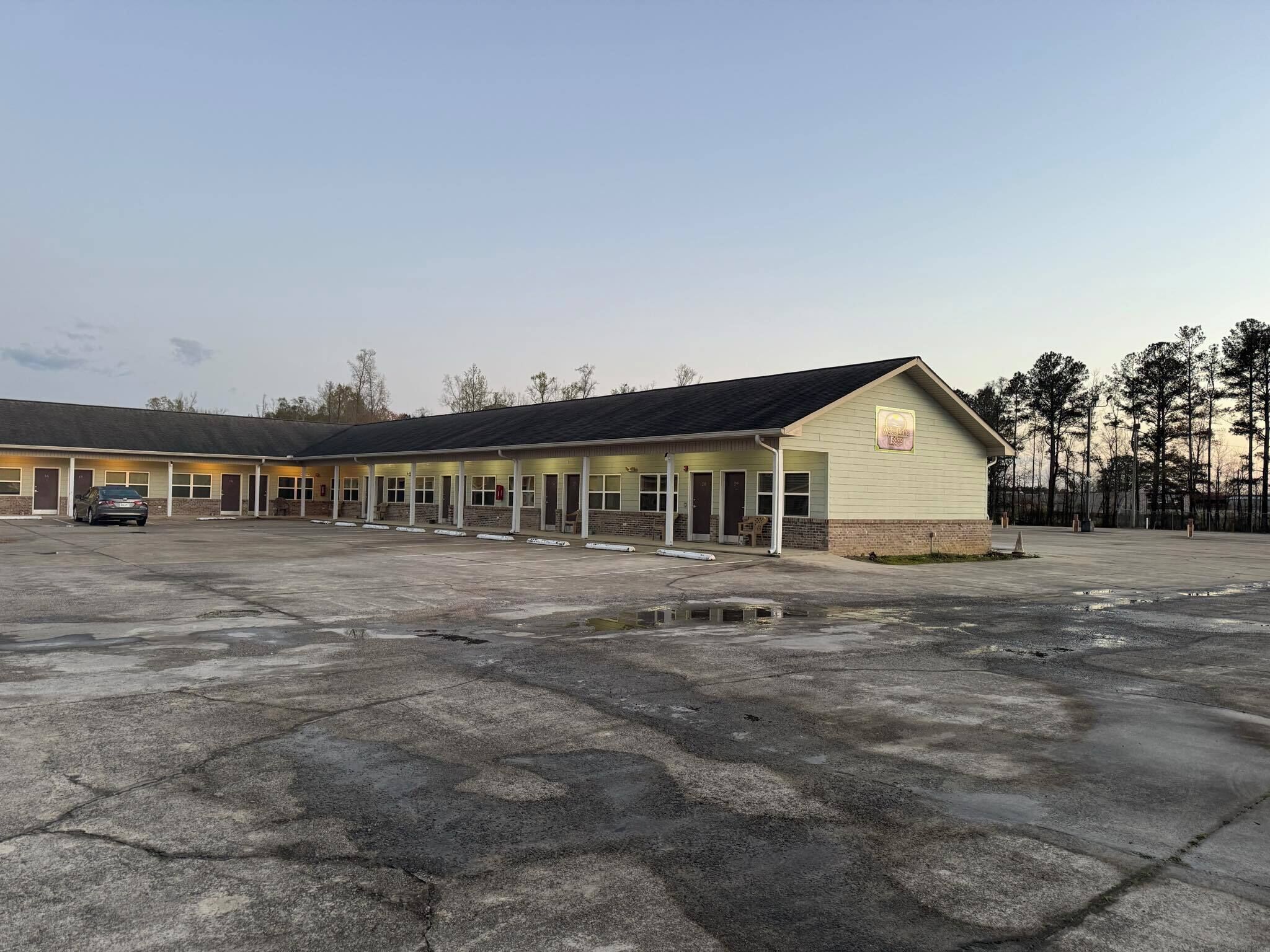 Un motel con una fila de habitaciones, una zona de estacionamiento techada y un pequeño espacio al aire libre para sentarse.