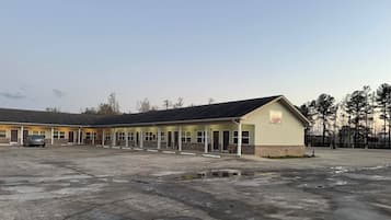 Un motel con una fila de habitaciones, una zona de estacionamiento techada y un pequeño espacio al aire libre para sentarse.