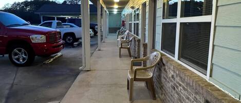 Corredor de motel com galeria coberta, fileiras de janelas individuais e estacionamento com vários veículos.