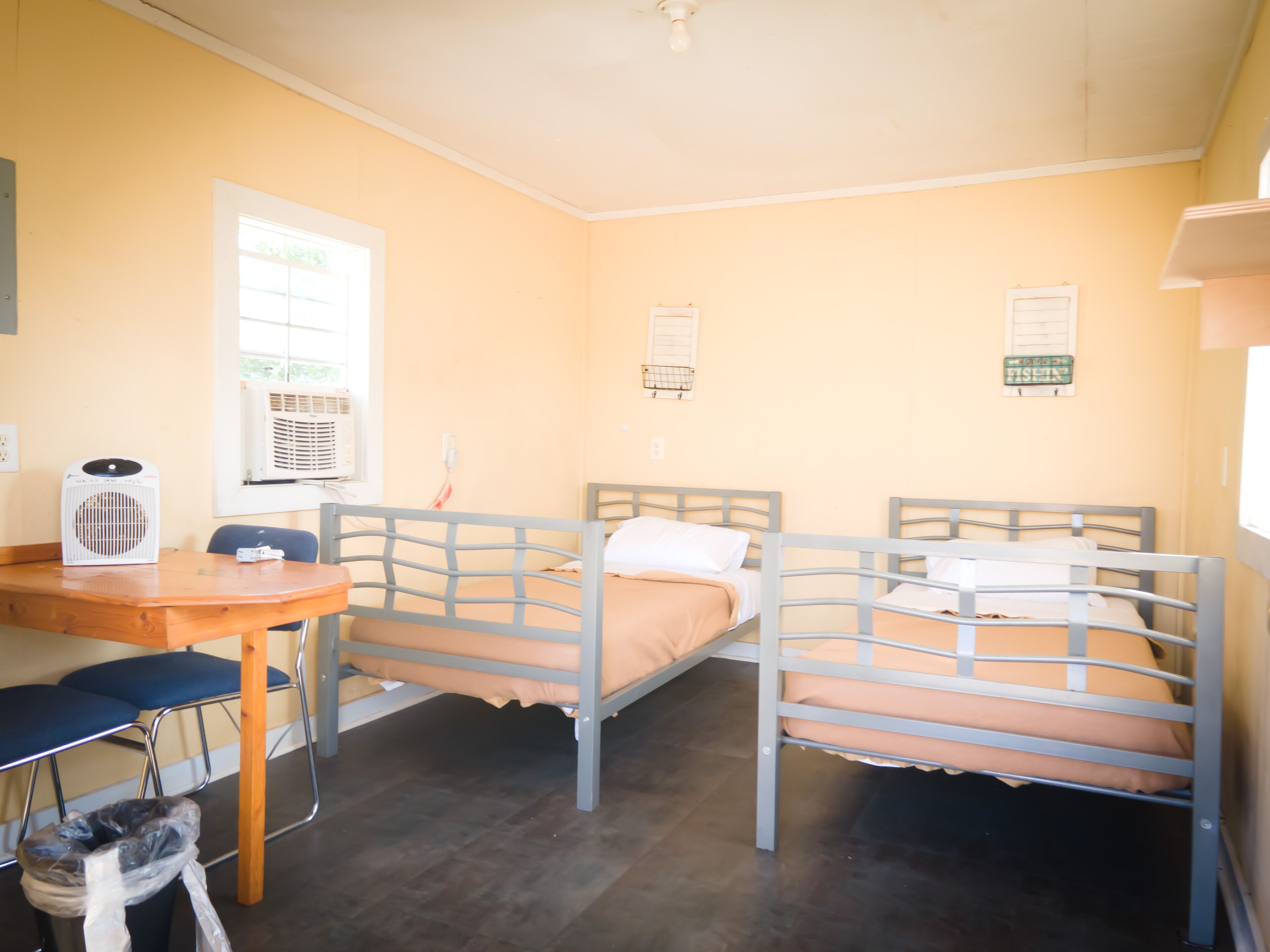 A room with two bunk beds, a desk, a chair, and a trash bin.