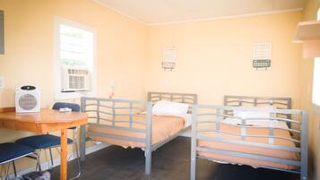 A room with two bunk beds, a desk, a chair, and a trash bin.