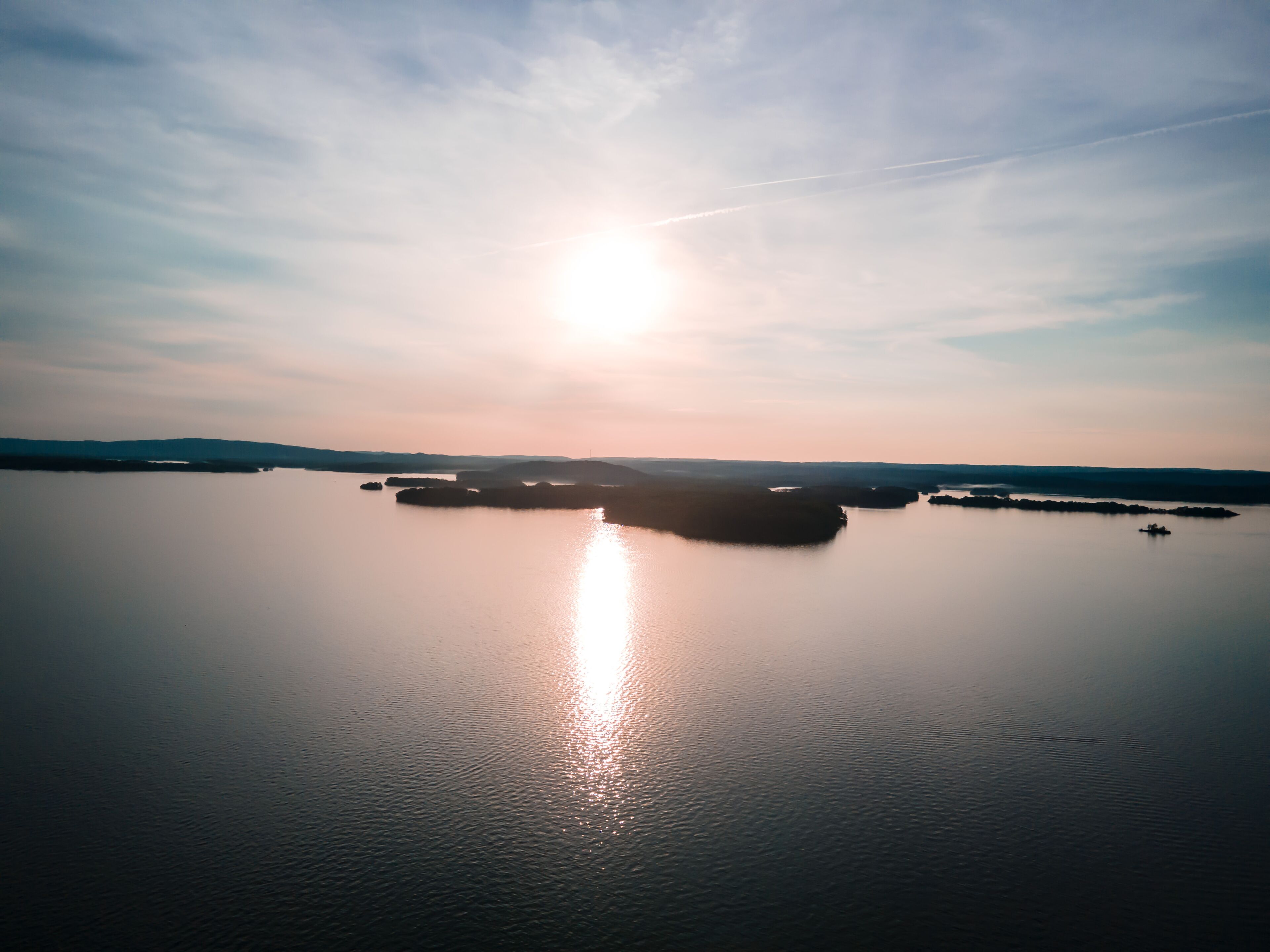 A calm body of water with a clear sky and a bright sun reflecting on the surface.