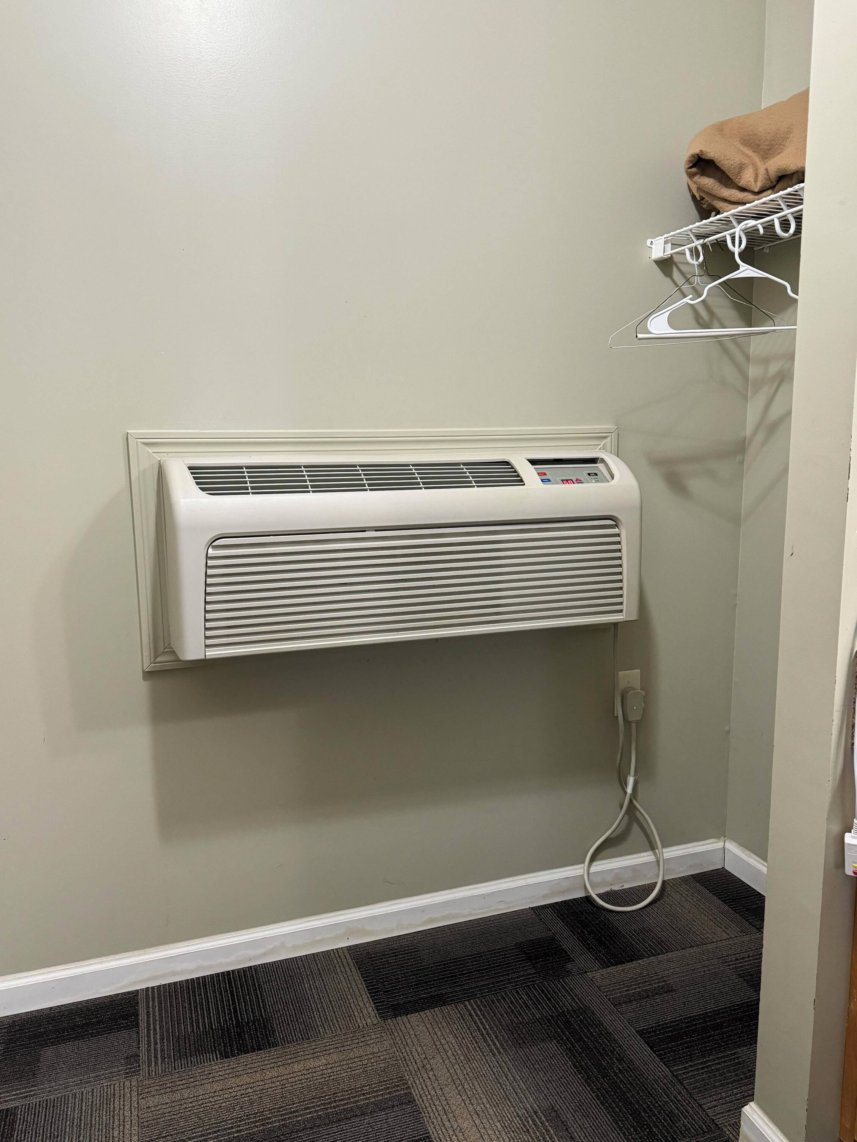 A bathroom with a wall-mounted air conditioner, a towel rack with a brown towel, and a patterned carpet.