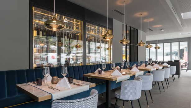 Een modern restaurant met donkerblauwe zitplaatsen, glazen vitrines en hanglampen.