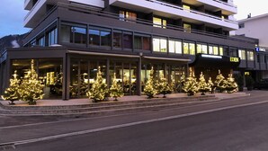 Een modern hotel met een glazen gevel, meerdere balkons en kerstbomen voor het gebouw.