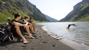 Vier personen zitten op een strand, met een berg op de achtergrond.