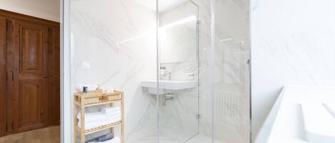 A modern bathroom with a glass-enclosed shower, a wooden shelf with towels, and a marble wall.