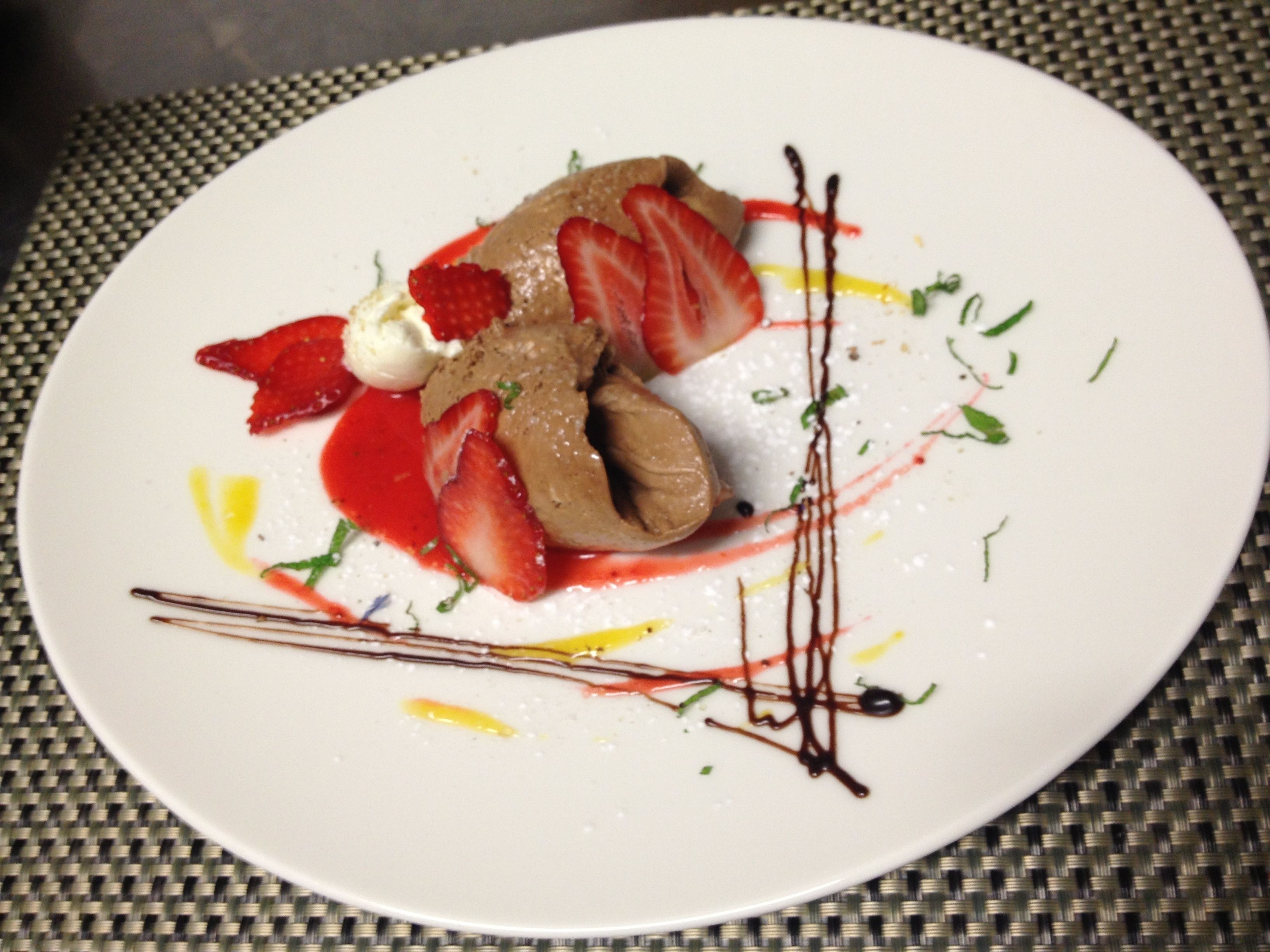 A dessert plate with chocolate mousse, strawberries, and a drizzle of sauce on a white plate.