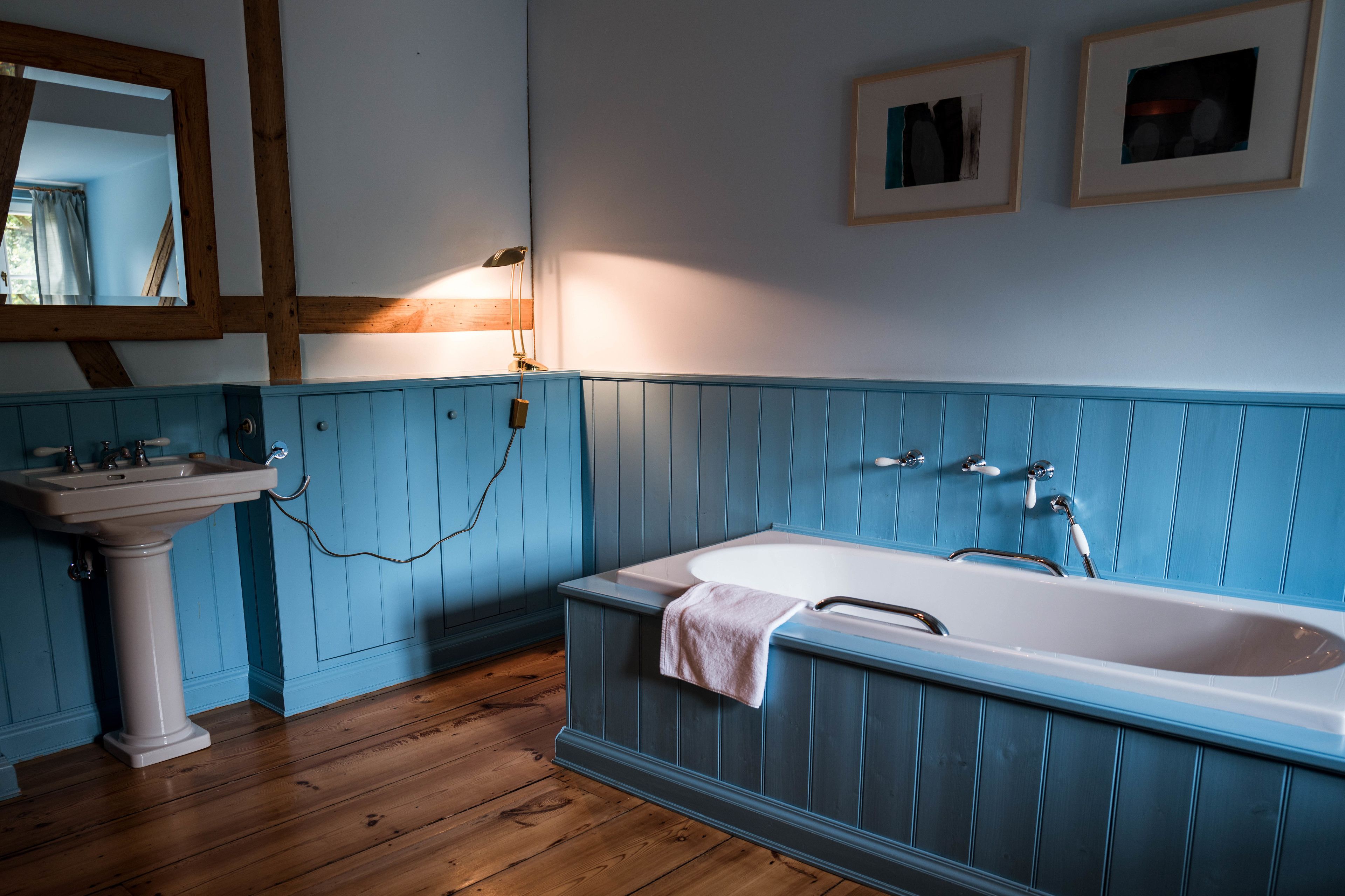 A bathroom with a wooden floor, a white sink, and a blue bathtub.