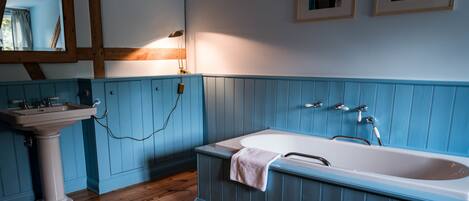A bathroom with a wooden floor, a white sink, and a blue bathtub.
