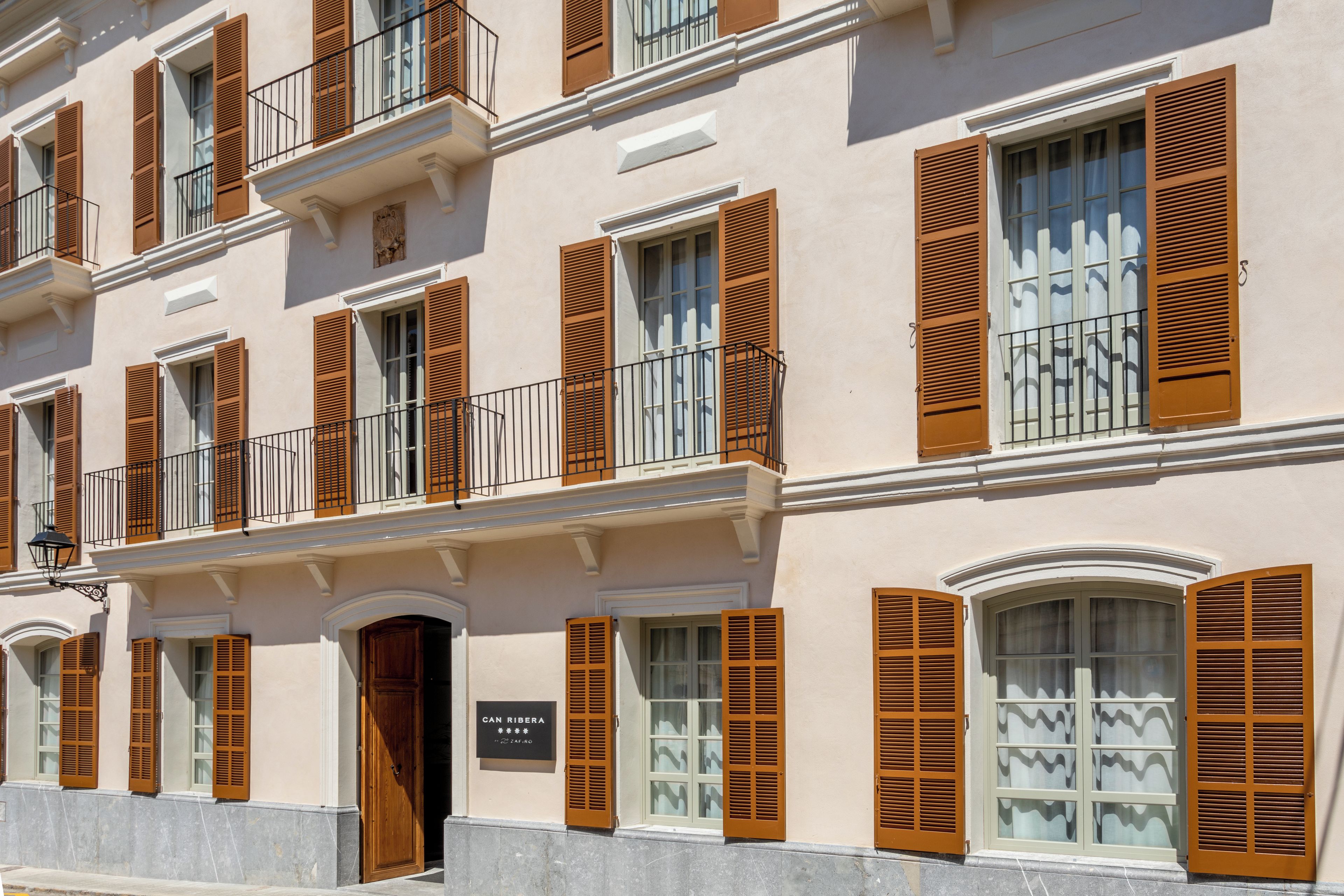 A multi-story building with balconies, wooden shutters, and a sign reading 'CAN RIBERA.'