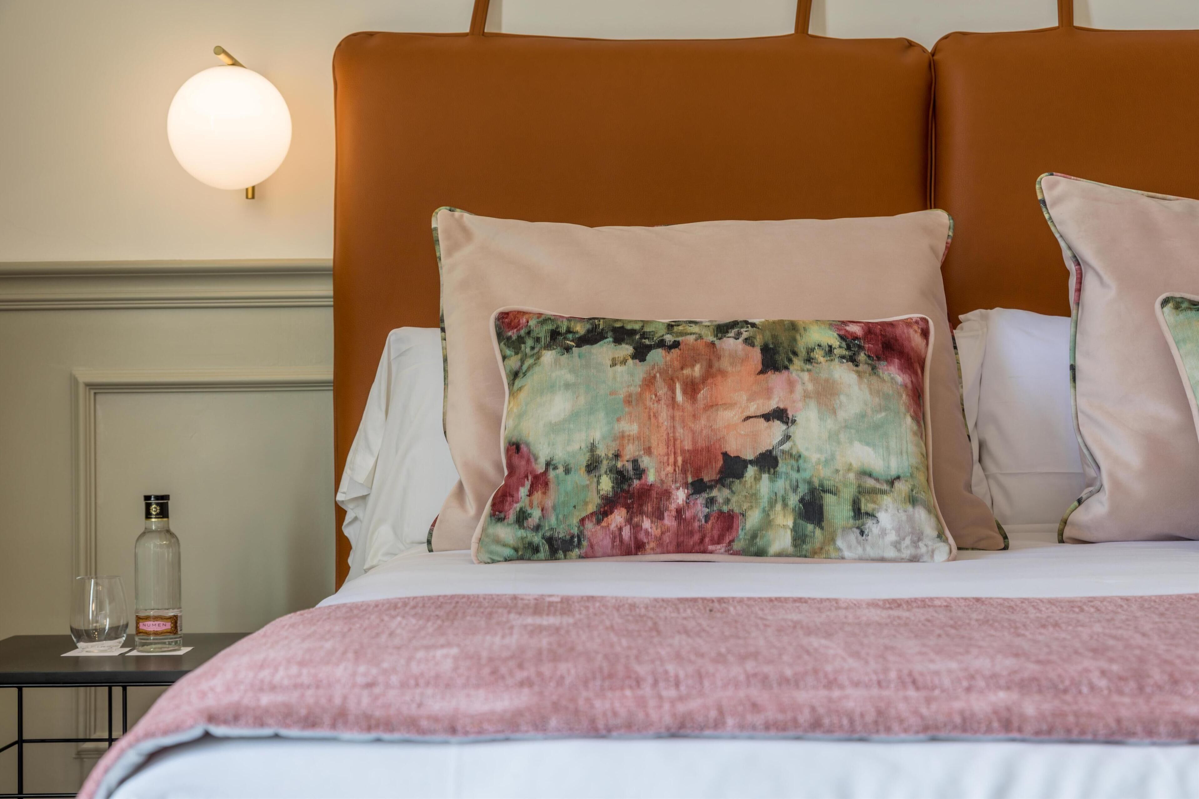 A bed with a floral pillow, a pink blanket, and a bottle of water on a nightstand.