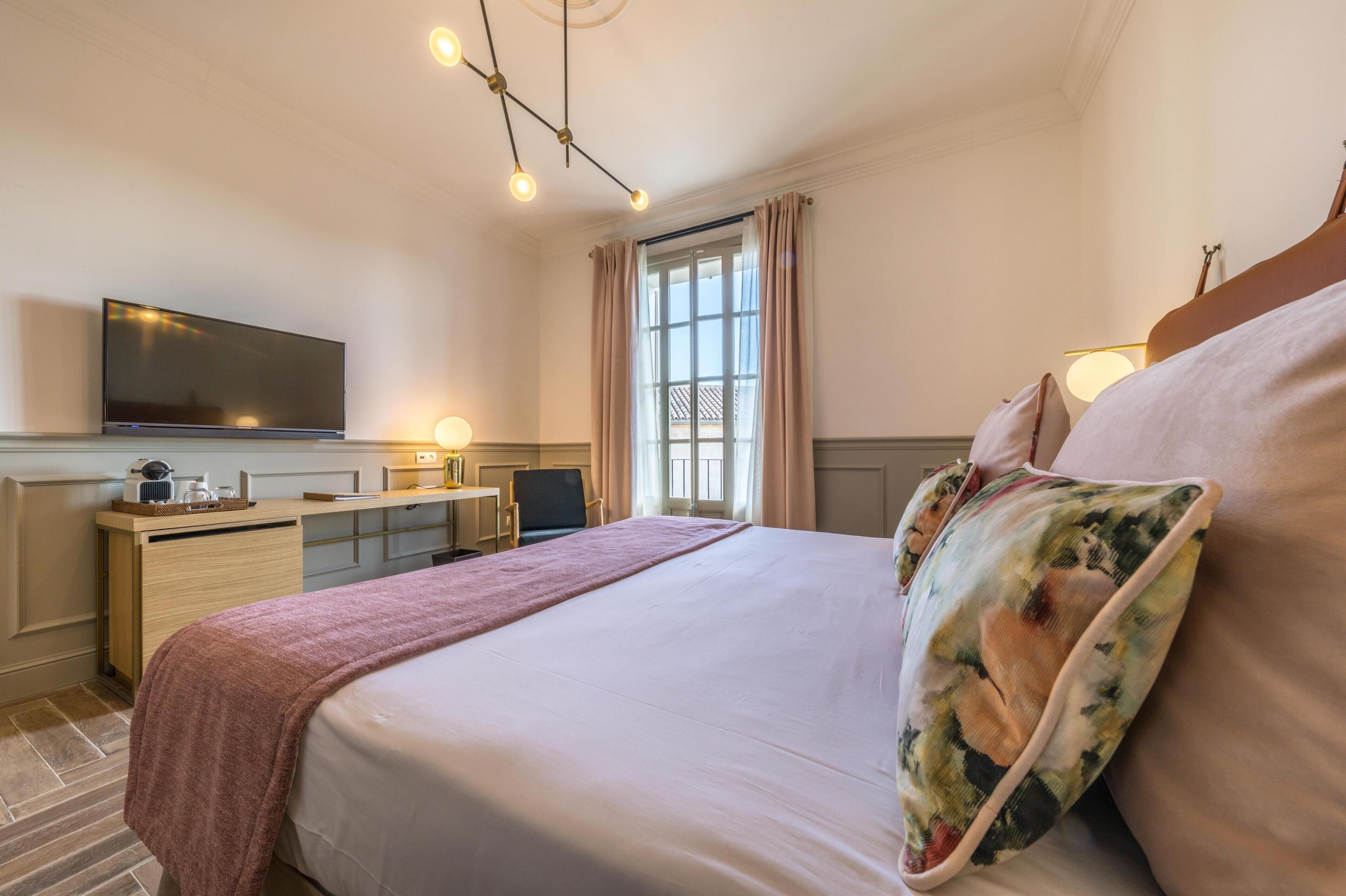 Habitación de hotel con cama, escritorio, televisión y ventana con cortinas.