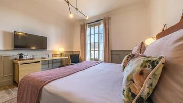 Habitación de hotel con cama, escritorio, televisión y ventana con cortinas.