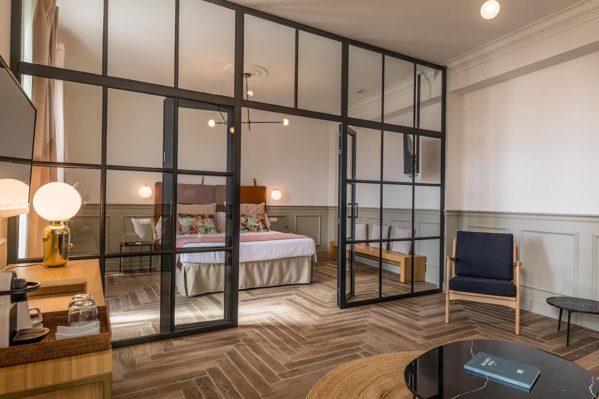 A hotel room with a large bed, a desk with a lamp, a chair, and a coffee table.